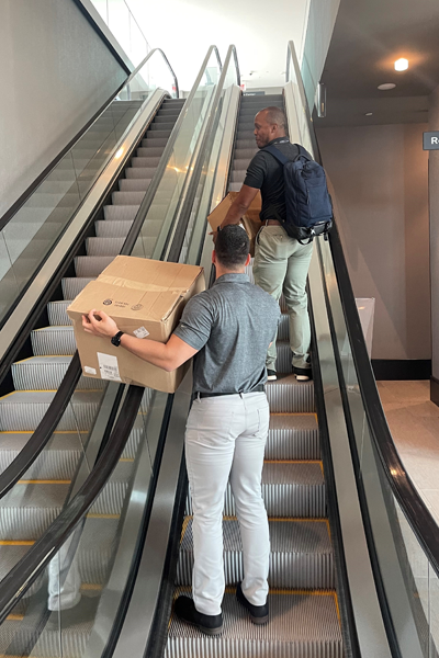 Two male residents carrying boxes up an escalator