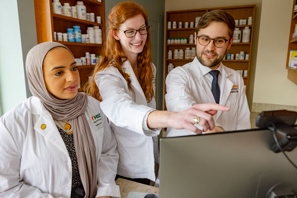 Three students work at at computer in a pharmacy setting.