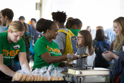 Woman serves food to a student at an event.