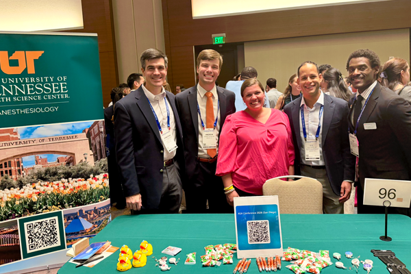 Group at a UTHSC Anesthesiology exhibit table with program materials and giveaways.