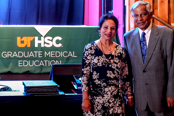 Male and female faculty member stading before a GME banner and table