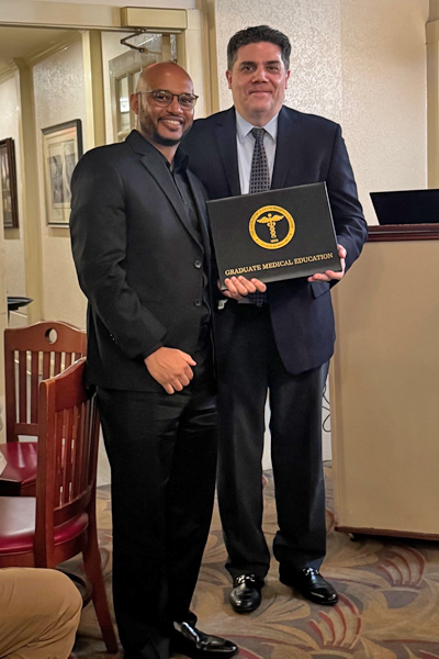 Graduate holding a certificate and faculty posing together