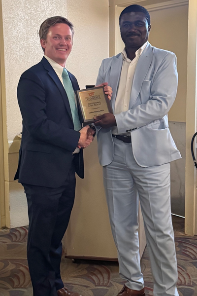 Graduate holding a plaque and faculty posing together