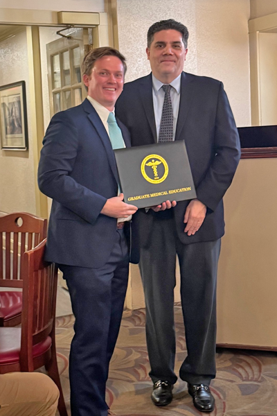Graduate holding a certificate and faculty posing together