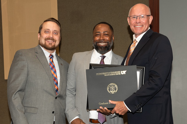 Resident holding a certificate with faculty at graduation
