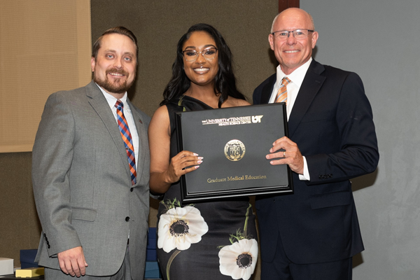 Resident holding a certificate with faculty at graduation