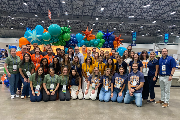 Everyone in front of a lighted sign with balloons