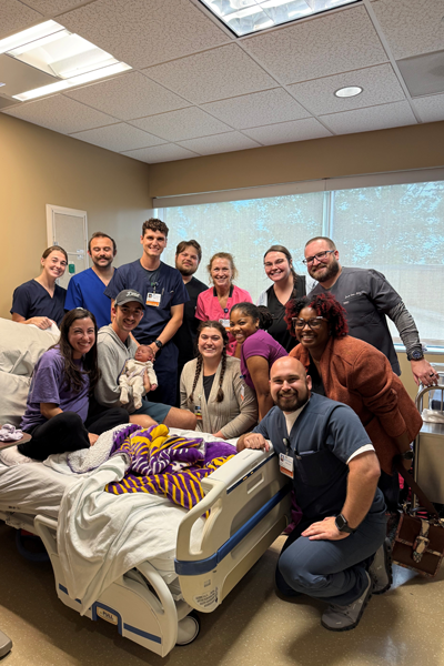 Female resident in a hospital bed in a room with her hubby and baby surrounded by fellow residents