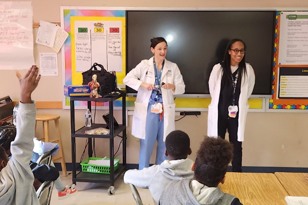 Med peds faculty/residents teaching in front of a room of the charter school students