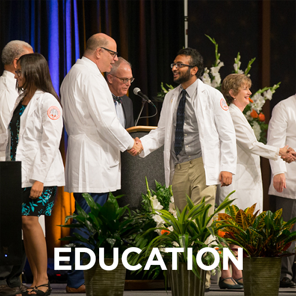 Male student shaking the dean's hand at white coat ceremony. The word "education" is imposed on the lower part of the image.