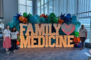 Residents at a conference in front of a lighted family medicine sign
