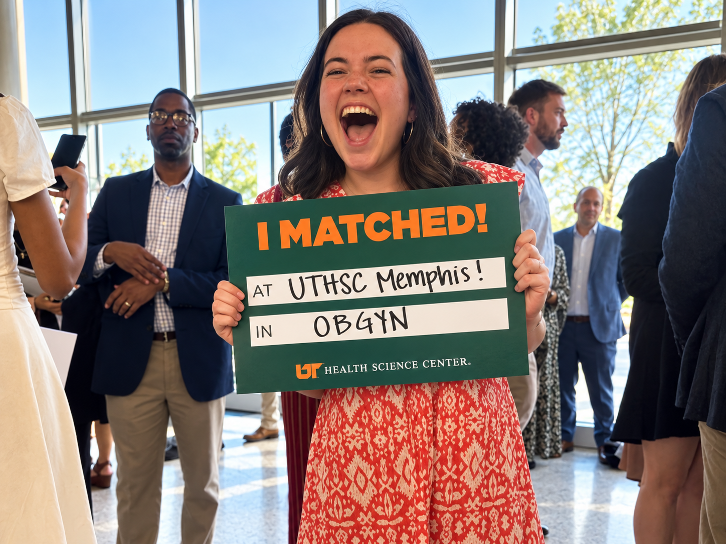 Future female resident in an orange dress holding a UTHSC matched sign