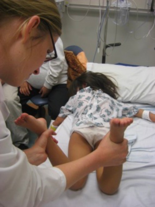 Little girl face down on a bed with a nurse raising her feet up