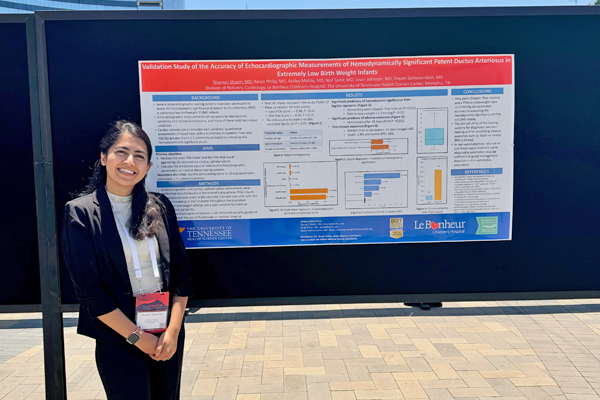 Female fellow standing before a research poster presentation outside