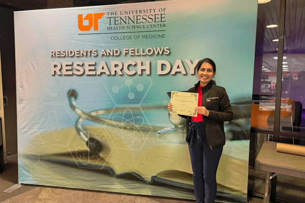 Female fellow holding a certificate in front of a Research Day banner