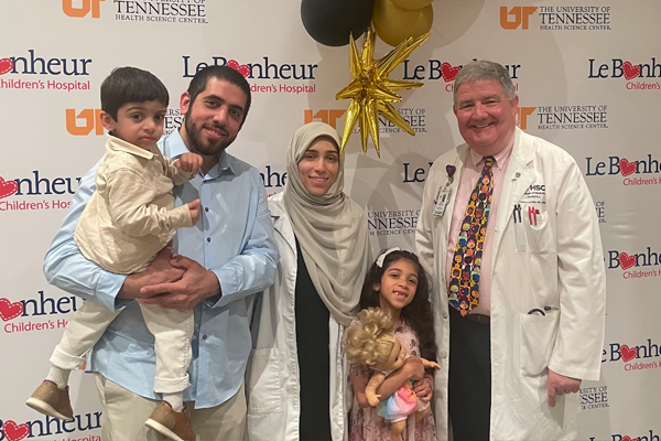 Fellow, their family, and a faculty member in front of a Le Bonheur background