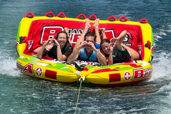 Three fellows riding an inflatable tube being towed across a lake