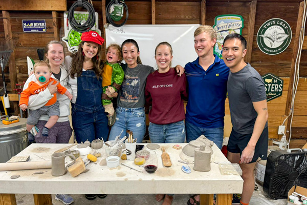 Group of adults and children posing behind a table covered with pottery tools and handmade ceramics